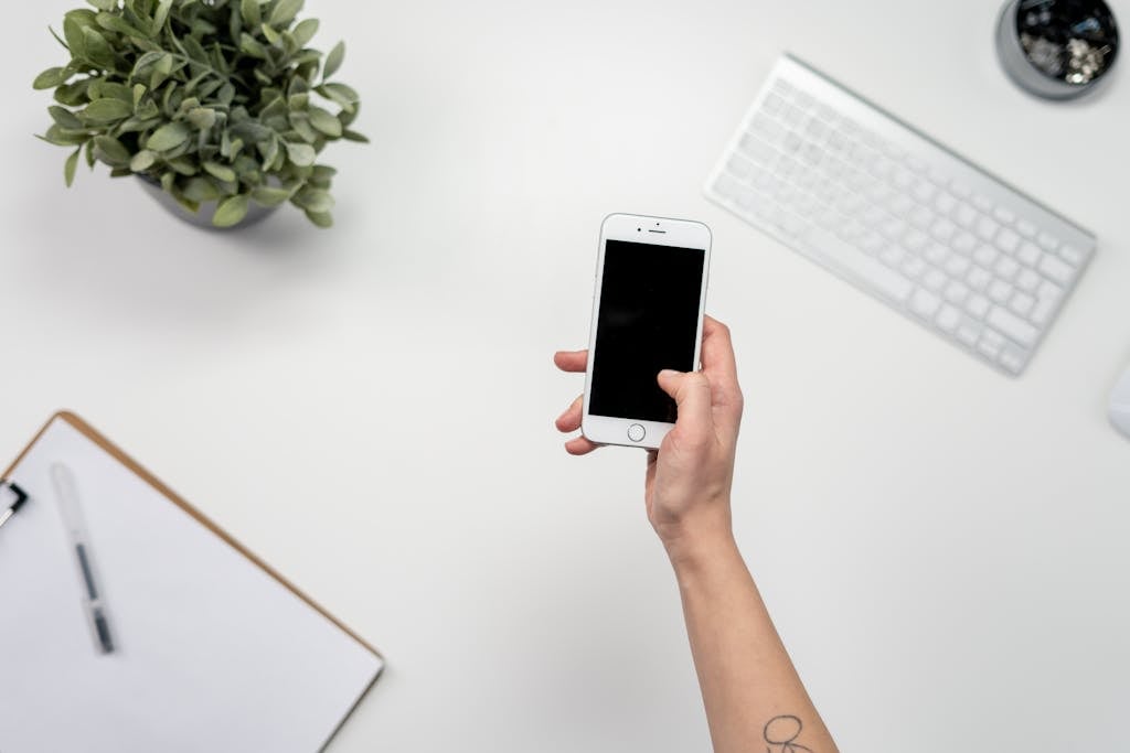 A clean and minimalist home office setup featuring a smartphone, keyboard, and plant.